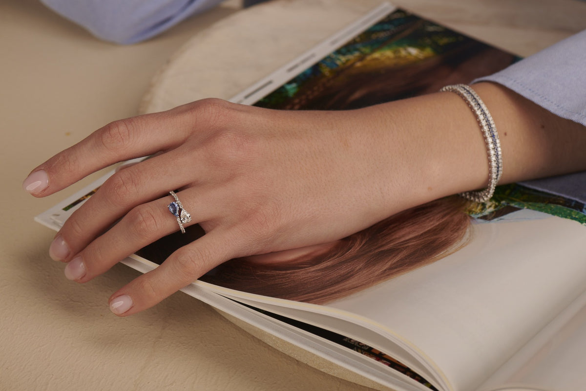 Deux – Blue Sapphire ring in white gold worn on the hand, resting on a book